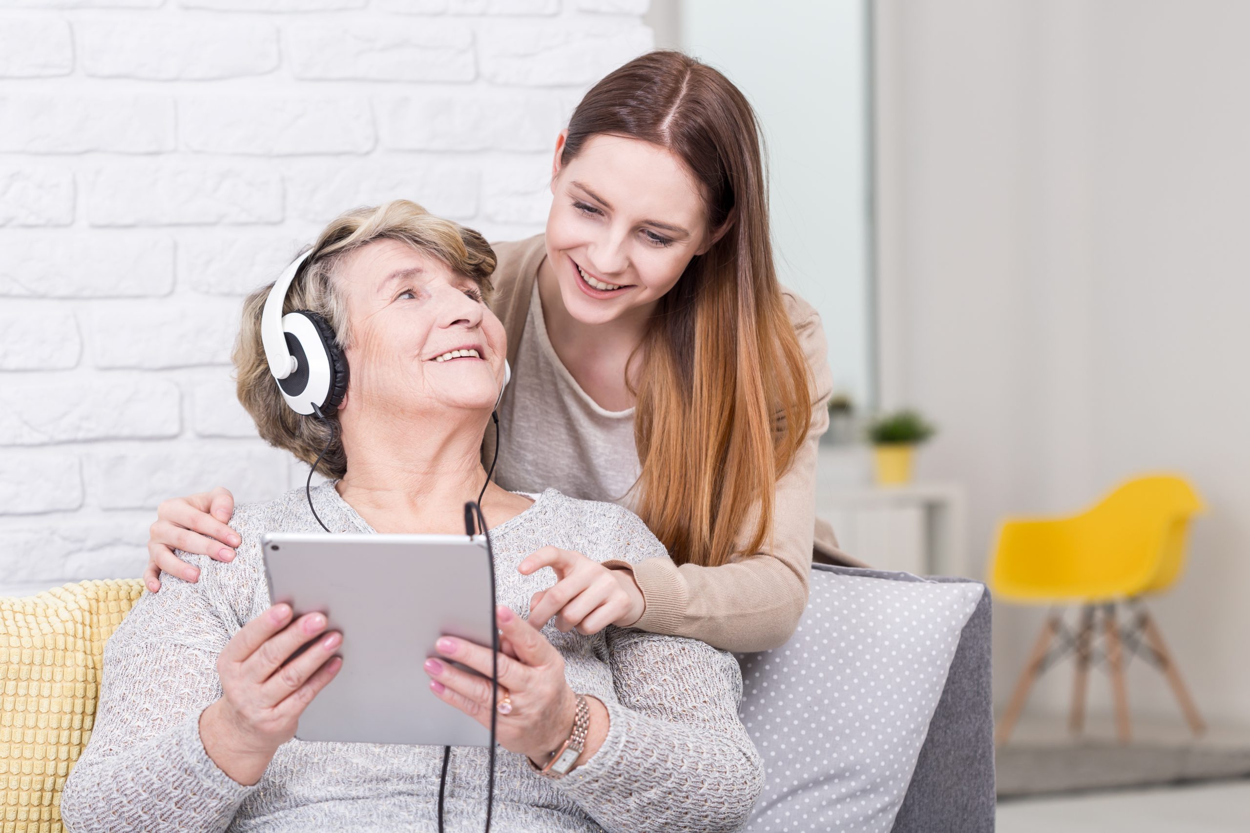 A young woman sits with an older woman as they watch a video together on a tablet