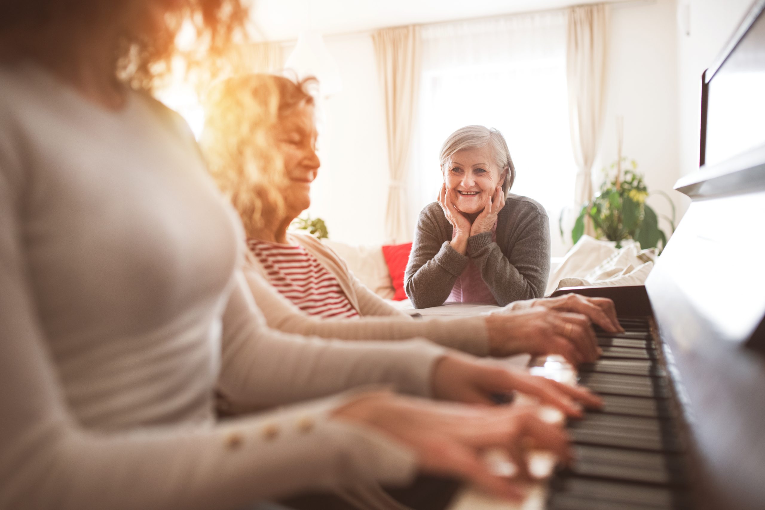 Caregivers and an older woman share a happy moment at a piano
