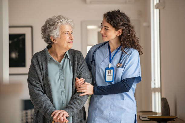 A nurse in scrubs walks arm in arm with an older woman